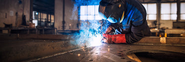 Man welding mild steel in factory wearing protective gear blue sparks flying